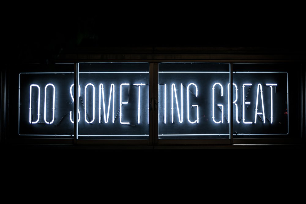 A neon sign against a black screen that says "Do Something Great"